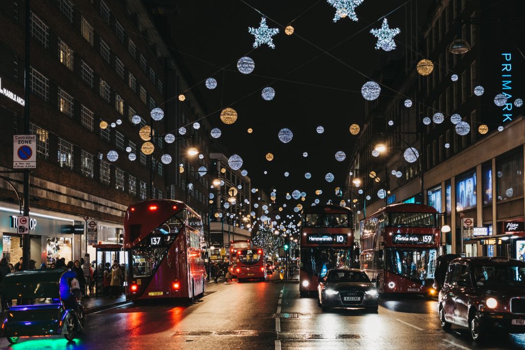 Vans and courier vans drive down a street under Christmas lights